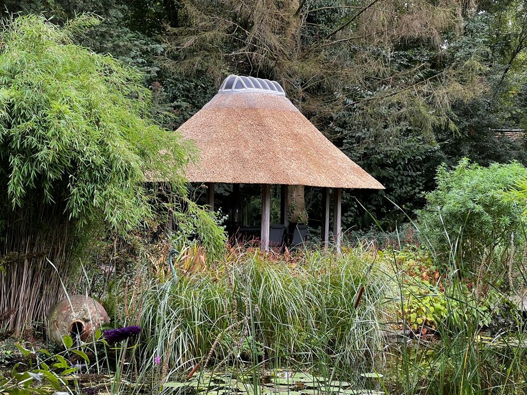 Rond rieten prieel met een lantaarn in een weelderige tuin met vijver