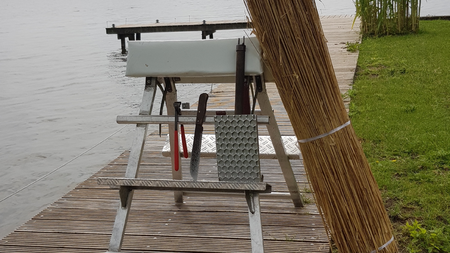 Bossen riet en een werkbok op een houten steiger aan het water